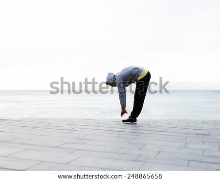 Young athletic man doing warm up before a morning run outdoors, full length of a young jogger stretching in the morning on a seaside