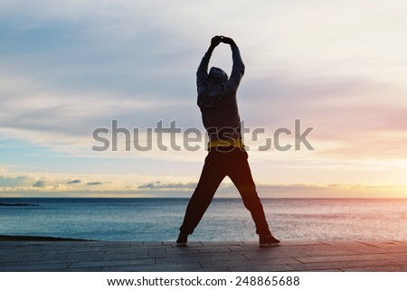 Full length silhouette portrait of a young jogger stretching in the morning and admiring beautiful view while standing on the beach