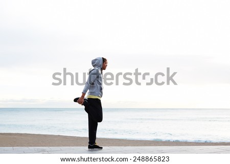 Young athletic man stretching his legs before a morning run, full length of a young jogger stretching in the morning on seaside