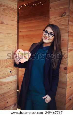 Portrait of cute girl in glasses holding little red gift box, enjoying present with romantic relationship, Valentine day, love and happiness concept