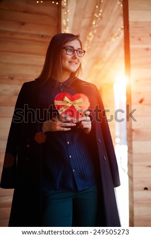 Portrait of elegant young woman holding red heart gift box presented by her boyfriend on Valentine\'s Day