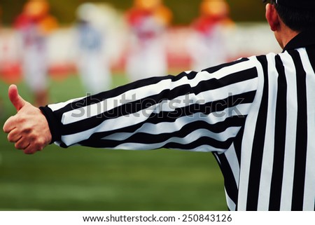 Referee of the american football on the field, american football referee gestures with big team in of focus on background