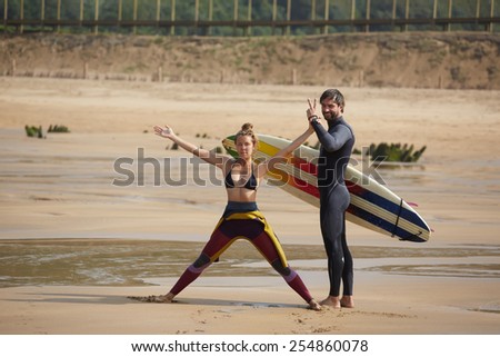 Beautiful young couple of surfers having fun standing on the beach at sunny day, girl and guy having fun during their summer vacation