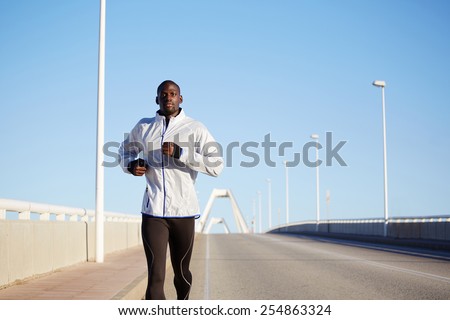 Half length portrait of black sportive man running on beautiful road over blue sky background
