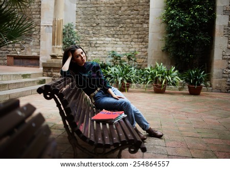 Full length portrait of pensive brunette hair woman sitting in beautiful spanish patio bench propping up her head with hands and look to the camera