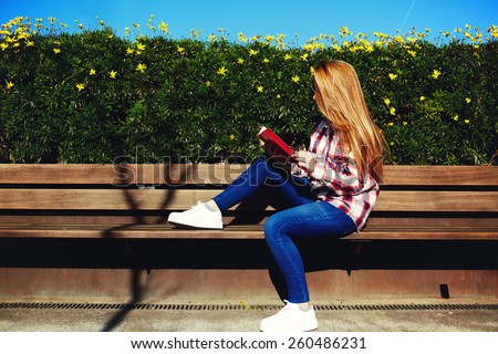 Charming girl relaxing in the spring park while read book, female student sitting on wooden bench at campus, attractive blonde hair young woman enjoying the sun at beautiful day outdoors