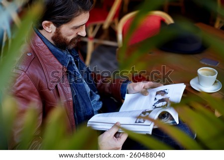 Portrait of attractive stylish man reading a magazine while drink coffee in coffee shop