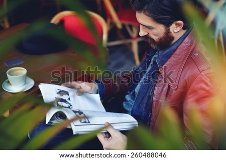 Portrait of handsome hipster man read magazine during his breakfast on the terrace of coffee shop, filtered image