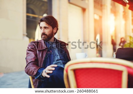 Portrait of handsome and stylish man with beard enjoying a cup of coffee in a coffee shop, adult fashionable hipster having coffee in beautiful cafe terrace at sunny day, flare sun light