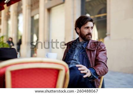 Portrait of handsome and stylish man with beard enjoying a cup of coffee in a coffee shop, adult fashionable hipster having coffee in beautiful cafe terrace