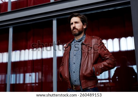 Portrait of fashionable mature hipster man dressed in pattern shirt standing indoors with hands in the pockets of leather jacket