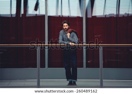 Full length portrait of stylish mature man standing interior beautiful big hall with glassy red color wall on background, male clothing designer, filtered image