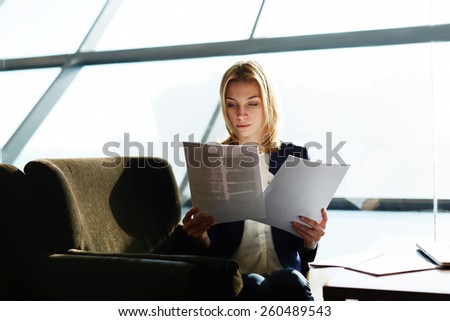 Portrait of attractive businesswoman reading papers or documents sitting in luxury coffee shop next to the window, soft focus, filtered image
