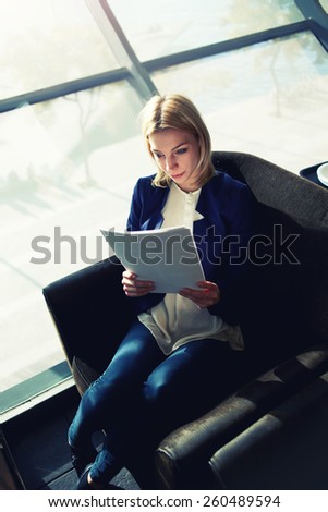 Top view portrait of young attractive businesswoman examining paperwork in bight light office interior sitting next to the window, business woman read some documents before meeting, filtered image