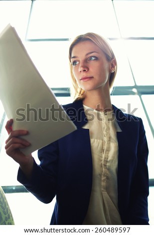 Low angle shot with young attractive businesswoman examining paperwork in bight light office interior sitting next to the window, business woman read some documents before meeting, filtered image