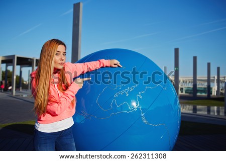 Portrait of young student girl pointing to the earth globe standing on school campus, science art globe object, attractive female teenager standing near big world globe outdoors