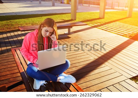 Gorgeous blonde hair female student focused and busy using laptop computer at campus, charming female teenager studying on park bench with open net-book and big copy space for text, exam preparation