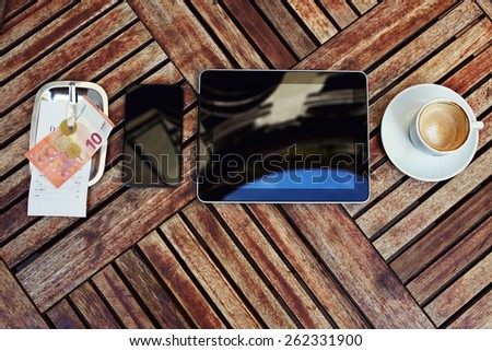 Top view mock-up with touch screen digital tablet, smart phone, bill check with money and cup of coffee on the wooden desk, gadgets with empty blank screen, work break of businessman