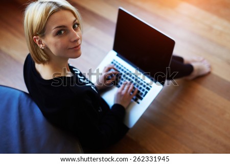 Lovely young woman working on laptop computer at home, attractive blonde hair student using laptop in her living room and look to the camera, female freelancer working at home