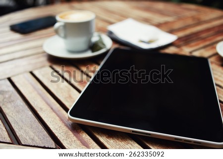 Wooden table with empty blank screen tablet, cup of coffee, cell phone and bill check with money, business work break