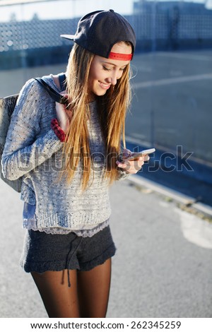 Gorgeous young woman wearing casual spring clothes walking down a city street while typing on her cellphone message, pretty girl walking outdoors in the street while using busy a smart phone