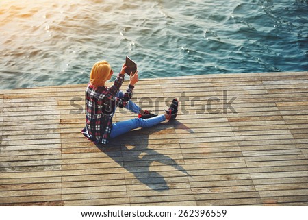 High angle shot of young tourist woman taking a photo of a beautiful view with her camera tablet, cute hipster girl relaxing at her sunny holiday photographing outdoors, young woman on sea pier, flare