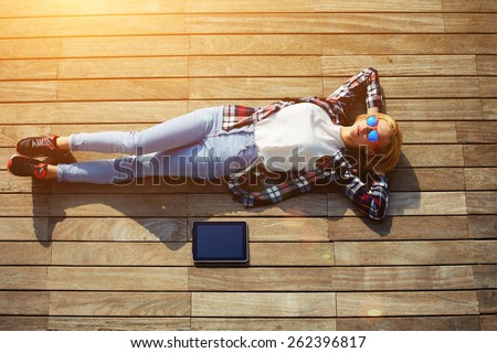 High angle shot of carefree young woman in summer glasses lying on the wooden jetty in the sun,young freelancer woman resting after work with digital tablet outdoors, enjoy her holiday or break, flare