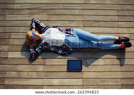 Attractive young woman enjoying sunshine while lying on the wooden pier with her tablet computer, female carefree freelancer girl resting after work outside, young female lying relaxed on a jetty