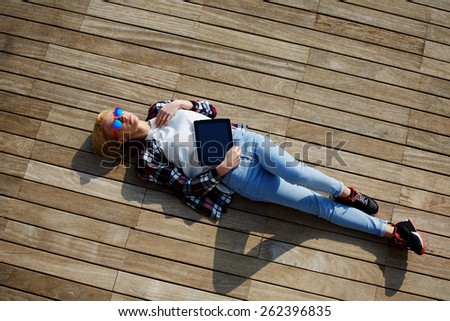 Attractive young woman enjoying sunshine while lying on the wooden pier with her tablet computer, female carefree freelancer girl resting after work outside, young female enjoy her holiday or break