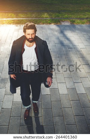 Portrait of elegant fashionable adult man dressed in coat walking in urban setting, stylish hipster man walking on the street at sunny evening, filter and flare sun