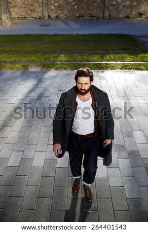 Portrait of elegant fashionable adult man dressed in coat walking in urban setting, stylish hipster man walking on the street at sunny evening