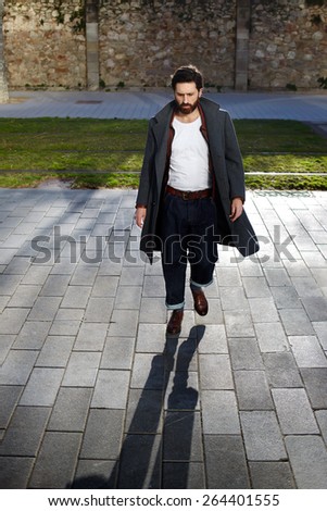 Portrait of elegant fashionable adult man dressed in coat walking in urban setting, stylish hipster man walking on the street at sunny evening