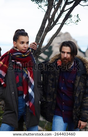 Portrait of stylishly dressed couple of hipsters posing in nature mountains landscape, handsome stylish man with beard and gorgeous brunette hair young woman, stylish couple in love posing outdoors