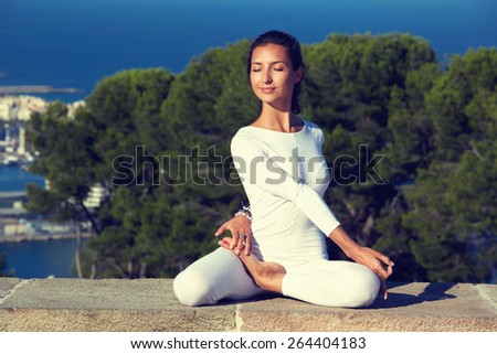Portrait of gorgeous young woman practicing yoga on a sunny day with amazing sea view from high altitude, woman seeking enlightenment through meditation, relaxed girl performing yoga routine, filter