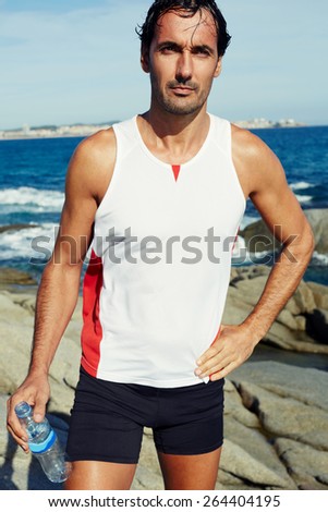 Portrait of mature runner standing on the rocks at sunny summer day, attractive male jogger standing on seaside while resting after intensive fitness training, fit man relaxing after workout outdoors