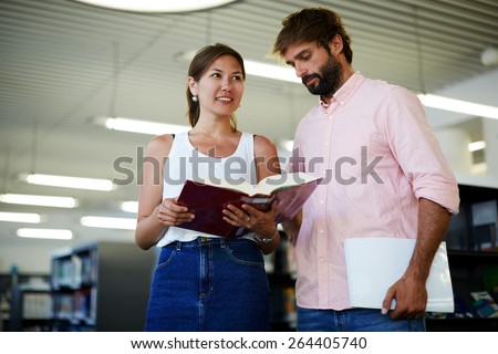 Portrait of young couple of students holding some books while preparing for university exams, business colleagues having fun while standing in modern work space, classmates studying in library
