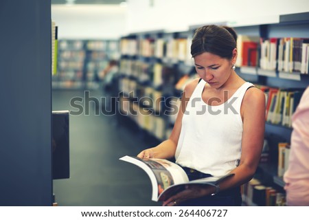 Portrait of young asian female holding open magazine or book while standing near bookshelves, attractive chinese student girl read book in university library, female freelancer in co-working space