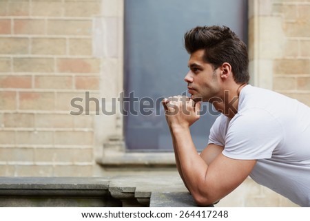 Side shot portrait of handsome man resting chin on clasped hands, confident man thinking about his choice, pensive man standing on brick wall background