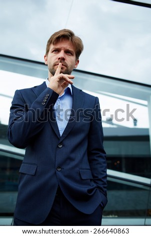 Portrait of caucasian businessman gesturing silence with his finger on his lips, man in suit shushing looking in front, man in suit with a finger in front of his mouth