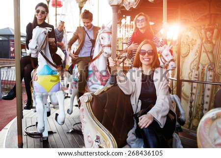 Girlfriends enjoying time together while riding on a merry go round during vacation holidays, group of attractive women having fun riding on carousel in amusement park