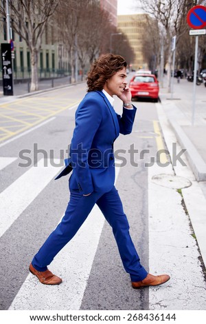Full length portrait of a young businessman talking on his mobile phone while walking in the street, man in suit walking down a city street having phone conversation