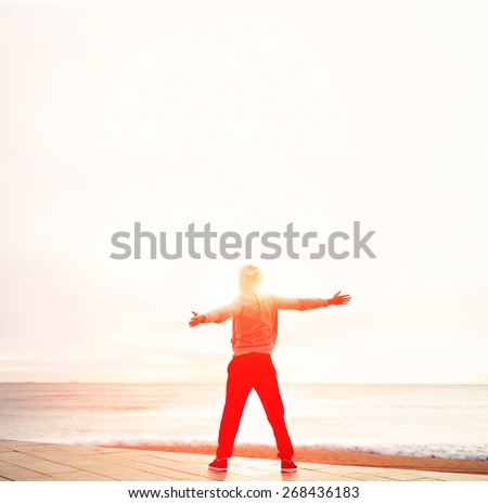 Freedom, relax and harmony in nature, full length portrait of sporty man with raised arms  standing next to the sea and enjoying amazing sunrise, happiness emotional concept