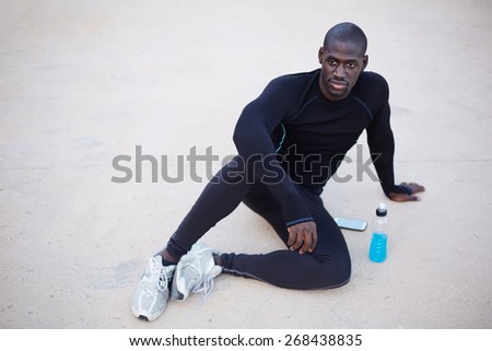 Smiling dark skinned runner resting after workout outdoors,male runner in active clothes taking break after run,active man having break after fitness training,confident sportsman looking to the camera