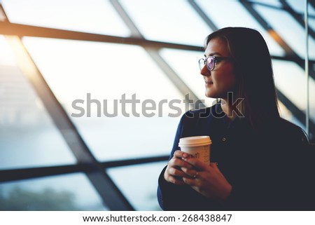 Portrait of beautiful cute girl sitting near big window with coffee take away in airport, filtered image