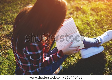 Pretty relaxed young woman reading a book at the lawn with sun shining