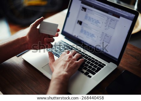 Side view of male hands holding credit card and typing text on laptop at home sitting at the wooden table, on-line shopping at home, cross process, focus on keyboard