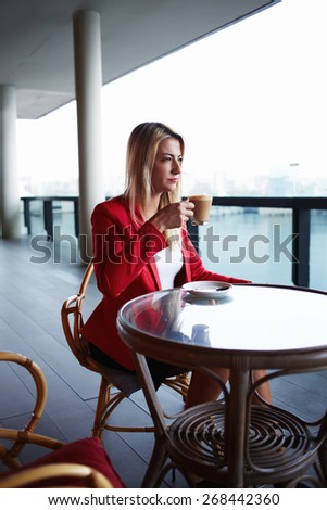 Young attractive businesswoman on a coffee break sitting at coffee shop table looking pensive and focused, beautiful elegant woman enjoying cup of coffee outdoors, thoughtful executive at lunch break