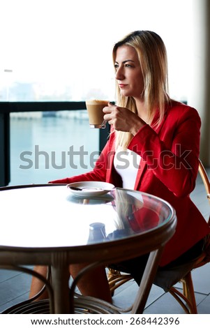 Young attractive businesswoman on a coffee break sitting at coffee shop table looking pensive and focused, beautiful elegant woman enjoying cup of coffee outdoors, thoughtful executive at lunch break