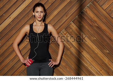 Attractive fit woman in sportswear listening to music with her headphones while training outdoors at beautiful sunny day, young female runner enjoying the sun while listen to music though earphones