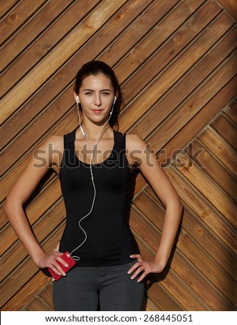 Attractive fit woman in sportswear listening to music with her headphones while training outdoors at beautiful sunny day, young female runner enjoying the sun while listen to music though earphones
